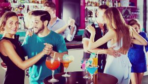 Young women with men are dancing in pairs оn the dance floor in the nightclub